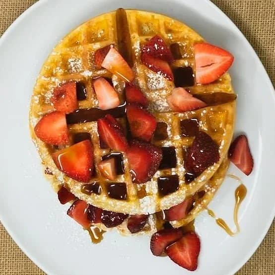 Golden waffle topped with fresh sliced strawberries and syrup.
